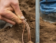 Close up picture of a hand installing electric ground rod